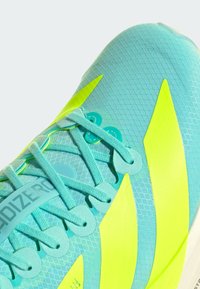 Svijetloplavi atletski tenisice s teksturiranim gornjim dijelom, neon žutim akcentima i prepoznatljivim dizajnom vezica. "Adizero" oznaka sa strane.