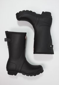 Botas de lluvia de goma negra con suelas texturizadas, de altura a media pantorrilla y correas laterales ajustables. Acabado liso con puntera reforzada.