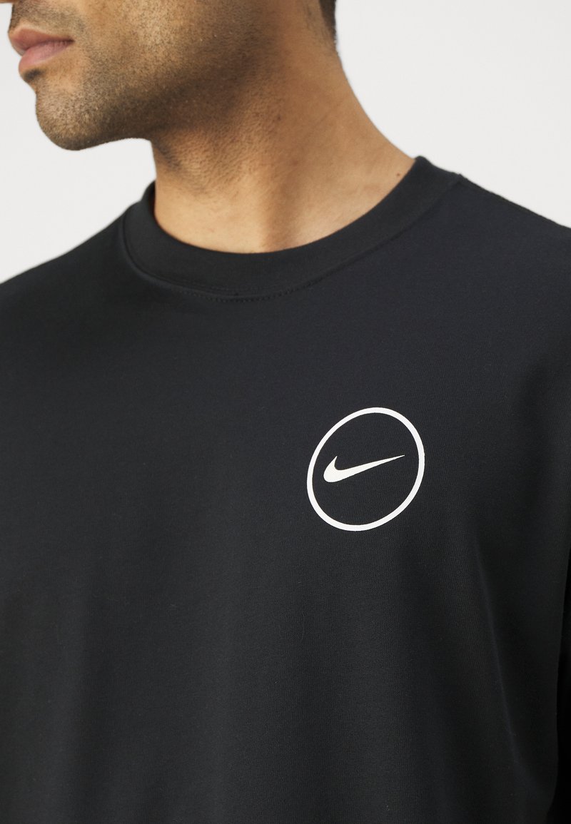 Schwarzes Nike-T-Shirt mit einem runden weißen Logo auf der Brust. Der Stoff wirkt glatt und hat ein klassisches Rundhalsdesign.