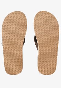 Mustat sandaalit, joissa on teksturoitu kumipohja ja beige jalkapodi. Pohjat näyttävät kuvioitua pinta, joka parantaa pitoa.