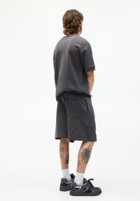Grijze katoenen t-shirt met korte mouwen, gecombineerd met bijpassende shorts. De shorts hebben een achterzak. Draagt dit met zwarte sportschoenen.