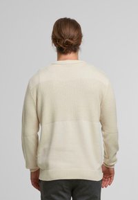 Maglione lavorato a maglia color crema con un motivo testurizzato sulla parte superiore della schiena e una sezione inferiore liscia. Polsini e orlo a coste.