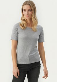 Grå bomulds T-shirt med korte ærmer, rund halsudskæring og tætsiddende pasform, præsenteret på en model mod en ensfarvet hvid baggrund.
