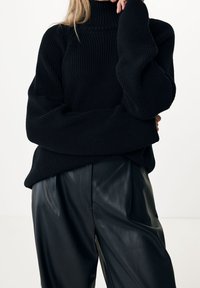 Pull en tricot noir à col roulé avec une coupe ample, un tissu texturé, des épaules tombantes et des détails côtelés ; associé à un pantalon en cuir noir taille haute.