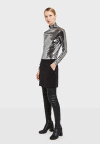 Metallic-silberner, taillierter Rollkragenpullover kombiniert mit einem schwarzen Minirock und schwarzen Overknee-Stiefeln. Glatte Texturen und strukturierte Silhouette.
