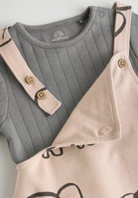 Grå ribbet langærmet top med rund halsudskæring kombineret med et lys pink overall med sorte abstrakte mønstre og træknapper.