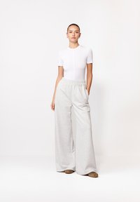 Biały bodysuit z krótkim rękawem w połączeniu z jasnoszarymi, szerokimi spodniami dresowymi z elastycznym pasem i bocznymi kieszeniami.
