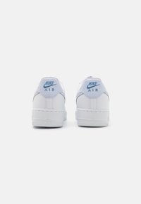 Ett par vita Nike Air-sneakers visade från baksidan med ljusblå Nike-logotyp på hälflikarna mot en vit bakgrund.