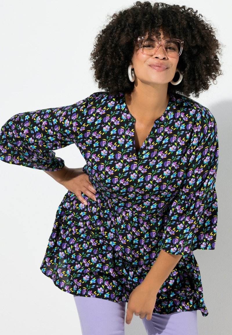 Blomstret bluse med sort baggrund, der har lilla og blå blomster, V-udskæring og udvidede trekvartærmer. Letvægtsstof.