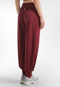 Bordeaux wijde sweatpants met een elastische tailleband, een gladde textuur en omgezoomde hemden, gecombineerd met lichtgrijze sportschoenen.