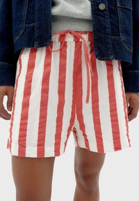 Shorts en coton rayés rouges et blancs avec une taille élastique et un cordon de serrage. Les jambes sont de longueur mi-cuisse et le tissu a une finition texturée.