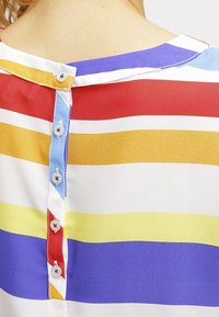 Dos d'un haut rayé coloré avec des boutons au centre, présentant des bandes horizontales rouge, jaune, blanche, bleue et violette.