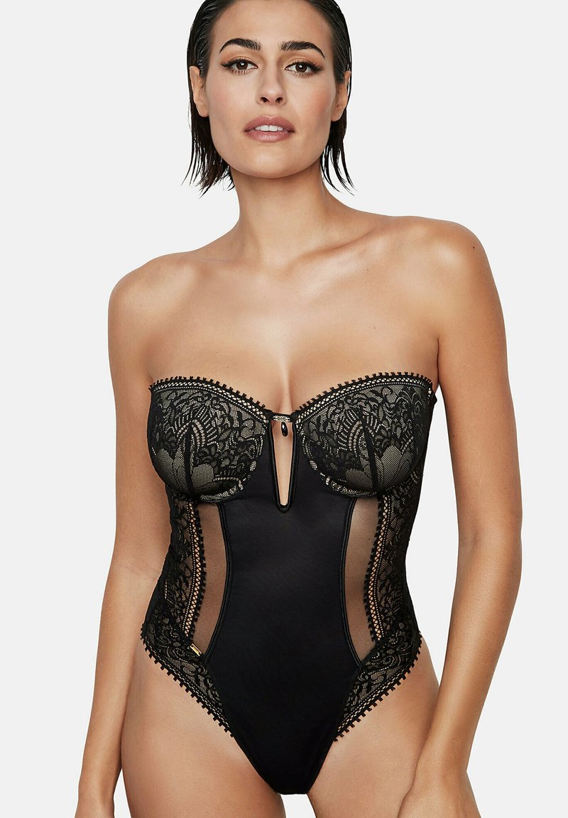 Zwart bodypak met kantafwerking, doorschijnende zijpanelen en een keyhole-ontwerp. Glad materiaal met fijn kantdetail op de buste.