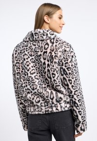 Leopardenprint nepbontjas met een brede kraag, elastische zoom en zachte textuur. Gestyled met donkergrijze strakke jeans.