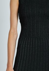Abito nero a coste realizzato in un materiale testurizzato con strisce verticali. Presenta un corpetto aderente e una gonna svasata, che brilla sottilmente.