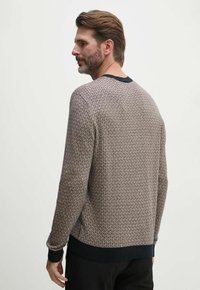 Maglione ai ferri con un motivo geometrico in beige e marrone, con un collo e polsini a costine di un blu scuro. La vista posteriore mostra una vestibilità rilassata.