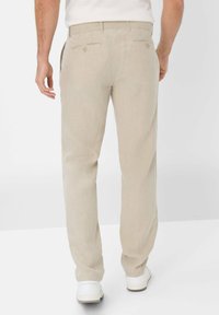 Light beige linen pants with a straight cut, two back pockets, and subtle texture. Worn with white sneakers, facing away from the view.