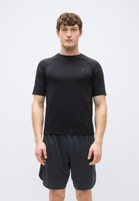 Svart tränings-T-shirt med korta ärmar i slät tyg, kombinerad med mörka mesh-shorts. Har en rund halsringning och en figursydd design.