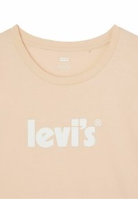Meruňková bavlněná tričko s kulatým výstřihem a bílým potiskem loga "levi's" umístěným uprostřed na hrudi. Hladká textura, neformální design.