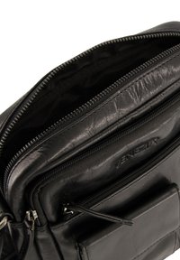 Schwarze Lederhandtasche mit mehreren Reißverschlussfächern, strukturiertem Oberflächen und geprägtem Logo. Glatte Oberfläche und robusten Reißverschlüsse sind sichtbar.