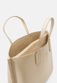 Borsa a tote beige realizzata in pelle testurizzata, con due manici, una tasca con cerniera e logo impresso sul davanti. Interno foderato in tessuto coordinato.