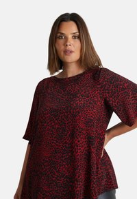 Top s leopardím vzorem v červené a černé barvě, krátké rukávy, volný střih, vyrobený z jemné látky, zaoblený výstřih, s mírně rozšířeným designem.