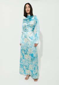 Abito lungo aderente con un motivo tie-dye blu e crema. Realizzato in satin, con maniche lunghe e un dettaglio annodato in vita.