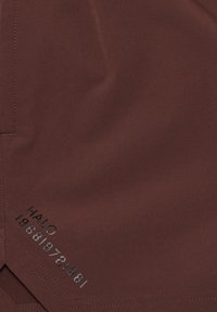 Brauner Stoff mit glatter Textur, der eine sichtbare Nahtdetail aufweist und in der Nähe der Ecke den aufgedruckten Text "HALO 198619721981" in Schwarz zeigt.