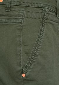 Tmavě zelené bavlněné kalhoty s hladkou texturou, oranžovým akcentovým knoflíkem a bočními kapsami s viditelným švem.