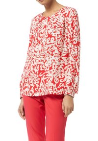 Blusa a maniche lunghe rossa e bianca a fantasia, con polsini arricciati e scollatura rotonda, realizzata in tessuto leggero e leggermente over-size.