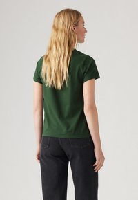Green, short-sleeved t-shirt made of cotton, featuring a crew neck and a relaxed fit, paired with dark, high-waisted denim pants.