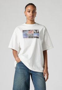 T-shirt branca oversize em algodão, com uma estampa gráfica de nove imagens a preto e branco e a cores, centrada no peito.