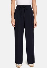 Pantalon large marine à taille haute avec un devant plissé, doté d'une ceinture à nouer. Le tissu semble lisse sans motifs visibles.