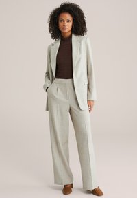 Svetlo sivi oblečen kroj s širokimi hlačami in strukturiranim blazerjem, kombiniran z rjavo teksturirano rolko in rjavimi čevlji.