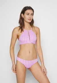 Conjunto de biquíni em xadrez rosa, apresentando um top de halter com recortes frontais e uma parte de baixo de cintura média. Tecido suave e design ajustado.
