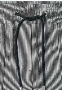 Tissu rayé vertical noir et blanc avec un cordon noir passant à travers des œillets argentés noué en un nœud lâche.