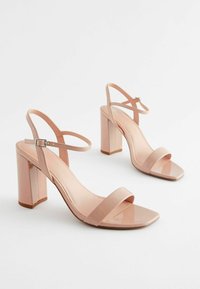 Pari ki kiilasi nude roosa mga sandal na may bloke na takong, may strap sa bukung-bukong at parisukat na dulo, sa puting likuran.