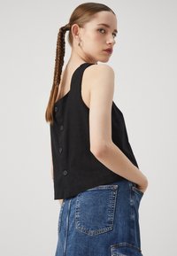 Black linen tank top featuring wide straps, a relaxed fit, and six decorative buttons down the back. Paired with denim bottoms.