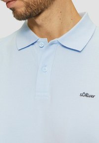Helles blaues Poloshirt aus strukturiertem Stoff, mit klassischem Kragen, einer Zwei-Knopf-Leiste und kleinem schwarzen gesticktem Logo.