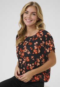 Juoda palaidinė trumpomis rankovėmis su viso paviršiaus gėlių raštu oranžinėmis ir raudonomis spalvomis; lengvas, laisvas audinys ir apvalus iškirpimas.