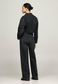 Chaqueta corta de mezclilla negra y pantalones de pierna ancha, con costuras clásicas y bolsillos traseros. Textura suave con un ajuste relajado.