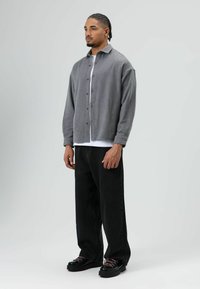 Grijs overhemd met knopen en kraag, gecombineerd met een wit T-shirt, zwarte loszittende broek en zwarte chunky schoenen met roze veters.