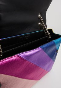 Multikleurige leren handtas met een geometrisch patchworkontwerp in roze, paars, blauw en zwart, met zilveren kettinghardware en een magnetische sluiting.