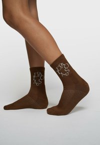 Chaussettes courtes en coton marron avec broderie de logo grise, texture côtelée et semelle renforcée pour un confort accru.