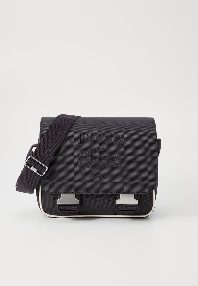 Black synthetic messenger bag with embossed logo, adjustable strap, metallic hardware, and cream-colored accents. Two buckle closures on the front.