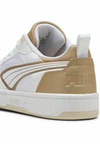 Hvid sneaker med guld accenter, glat syntetisk materiale, snørebåndsdesign, polstret krave og prægede logo på hælen.