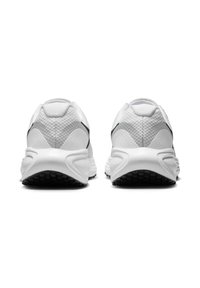 Zapatillas deportivas blancas con parte superior de malla texturada, tacón redondeado y suela de goma negra. La vista trasera muestra un diseño minimalista y acentos en contraste.