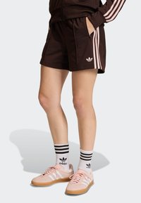 Brown athletic shorts featuring pink side stripes, a logo on the right leg, and side pockets, paired with pink shoes and striped socks.