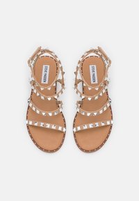 Sandales plates Tan de Steve Madden avec multiples lanières, clous pyramides argentés, fermeture à boucle à la cheville et design à bout ouvert.