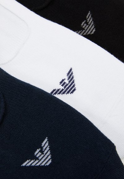 Trois paires de chaussettes en blanc, noir et marine, ornées d'un petit logo rayé diagonal dans des couleurs contrastées sur chacune. Texture en tricot douce.